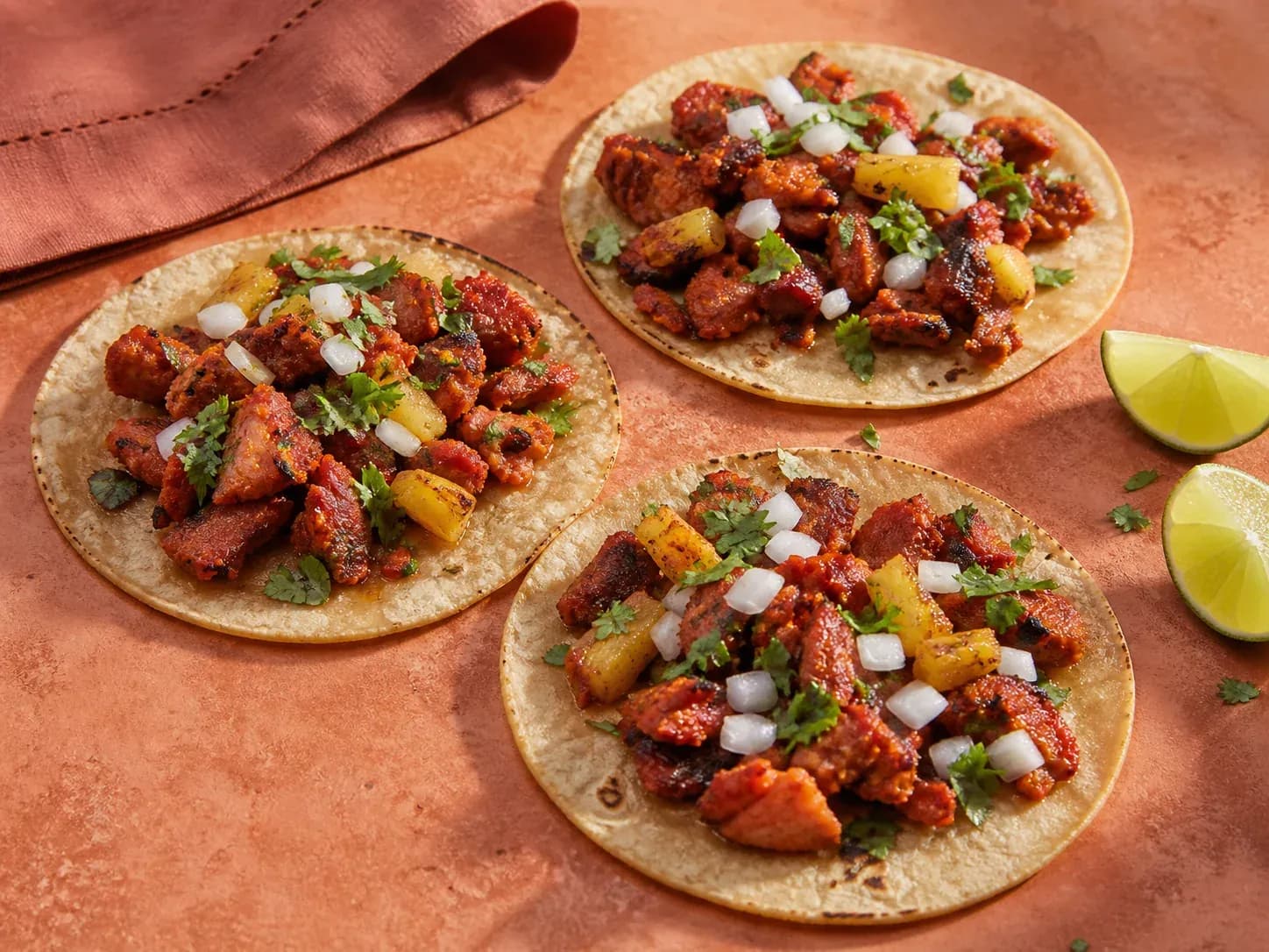 Three tacos al pastor with charred pork, pineapple, onion, cilantro, and lime